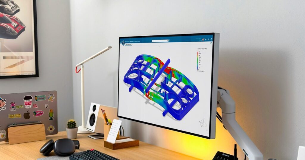 A modern workstation with a monitor displaying a structural simulation analysis in SIMULIA, showing stress distribution on a mechanical part in a color-coded FEA visualization.
