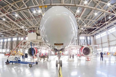 A front-facing view of a commercial airplane inside a spacious, well-lit maintenance hangar.