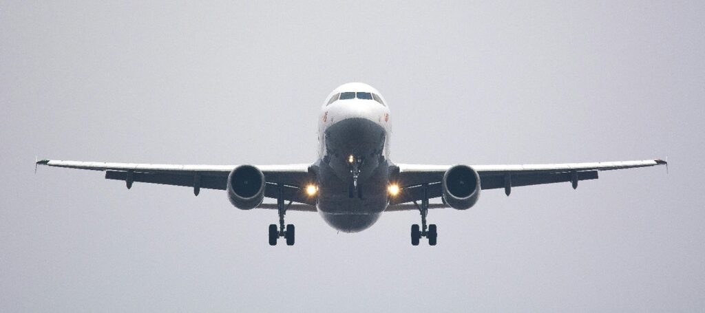A commercial airplane approaching for landing, viewed head-on against a gray, overcast sky.